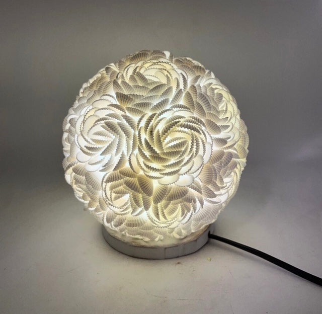Cette lampe, réalisée à la main par des artisans talentueux, prend la forme d'un globe délicat orné de coquillages naturels. Ces coquillages, agencés en roses fines et serrées, créent un motif élégant et raffiné. Chaque élément est minutieusement disposé pour offrir une harmonie parfaite et une beauté intemporelle.

Reposant sur une base en bois, la lampe apporte une touche de chaleur et de naturel à votre intérieur, créant une ambiance douce et accueillante. 